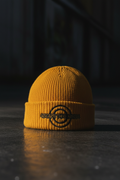 ETN Cable Beanie Limited Drop — mustard yellow with navy embroidered logo on dark concrete, editorial streetwear photography